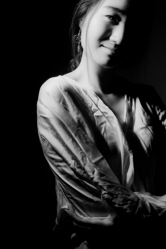 A black and white portrait of a young woman with a pensive expression, her face partially obscured by shadows and her body wrapped in a flowing garment.